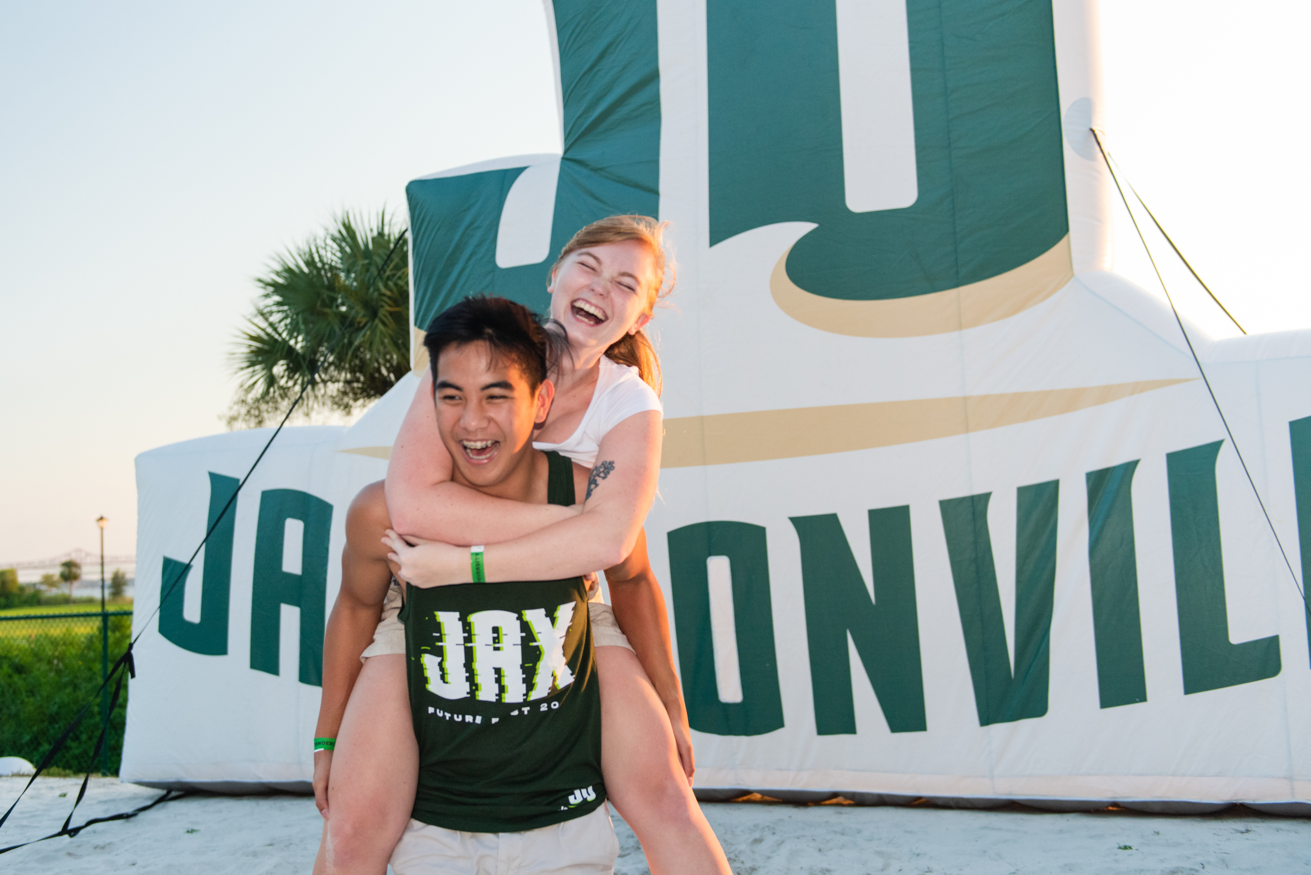 Two students piggy-backing in front of a JU inflatable.