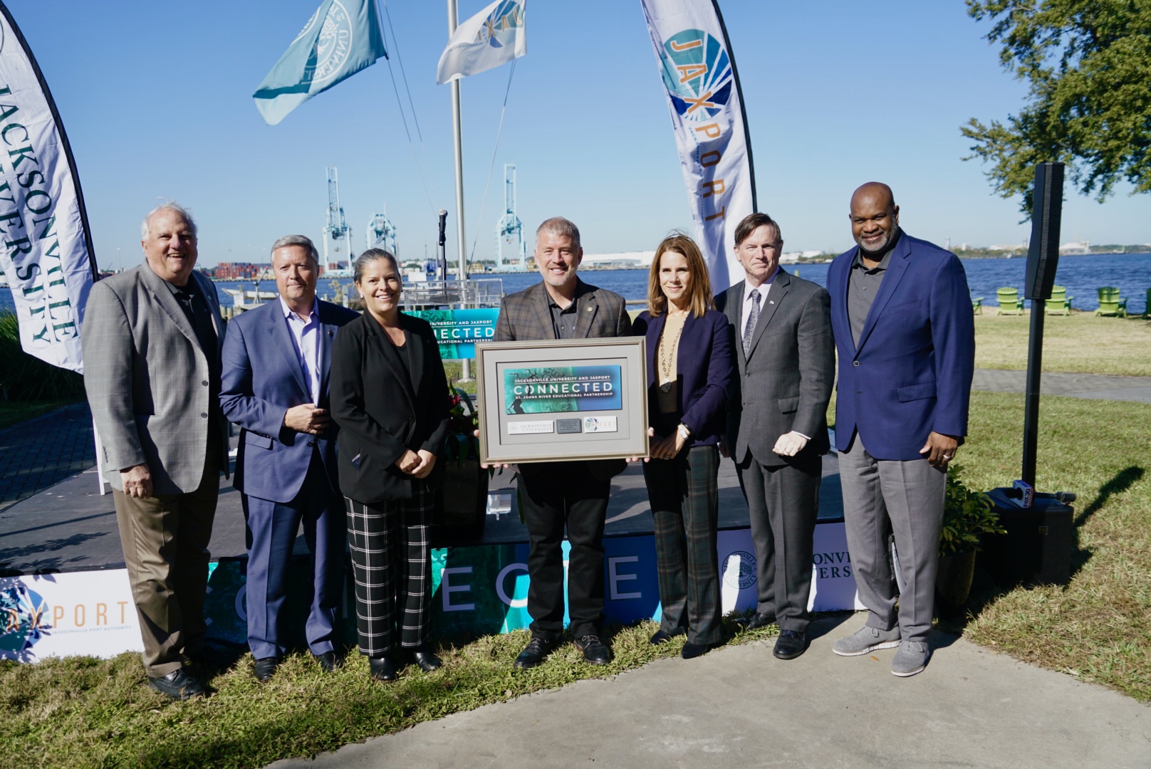 A group of Executives holding a Connected plack at Jacksonville University St John's River docs.