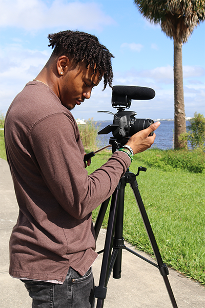 Male student filming on the river with a camera on a tripods.